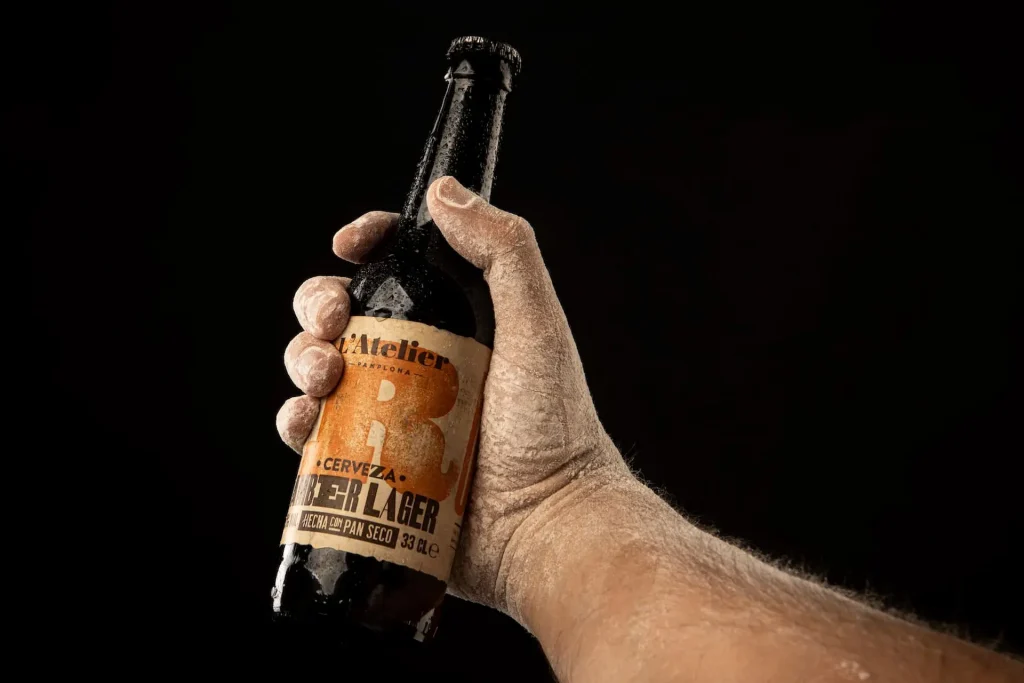 Detalle de la mano de una persona sosteniendo una cerveza y su respectivo diseño de la etiqueta de Cervezas L'Atelier