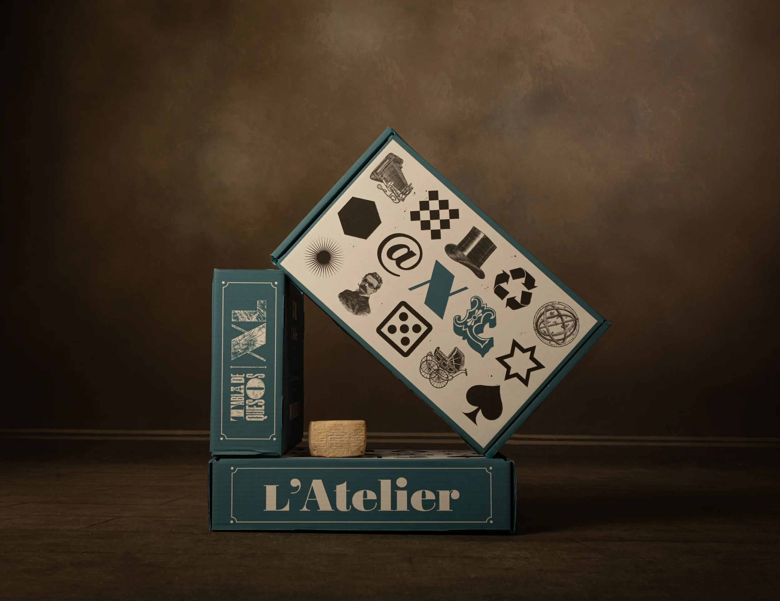 Imagen de laterales de varias cajas apiladas con detalle azul con el diseño de packaging de quesos L'Atelier con tipografía e iconografía de letterpress
