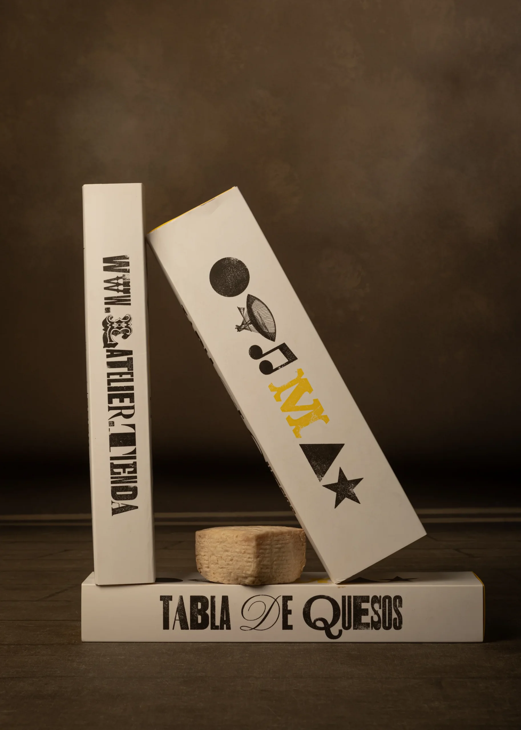 Imagen de laterales de varias cajas apiladas con detalle amarillo con el diseño de packaging de quesos L'Atelier con tipografía e iconografía de letterpress