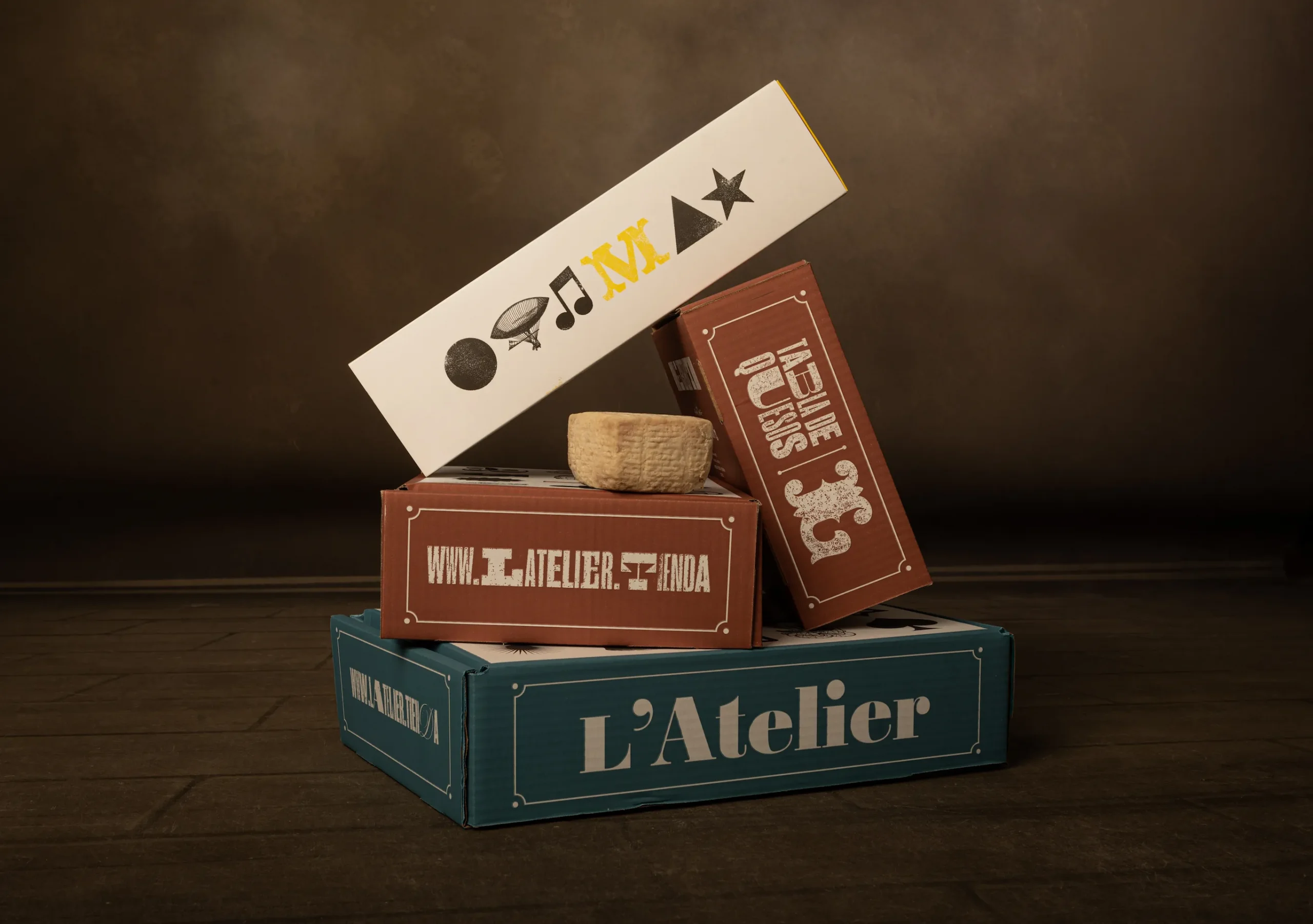 Imagen de varias cajas apiladas con el diseño de packaging de quesos L'Atelier con tipografía e iconografía de letterpress