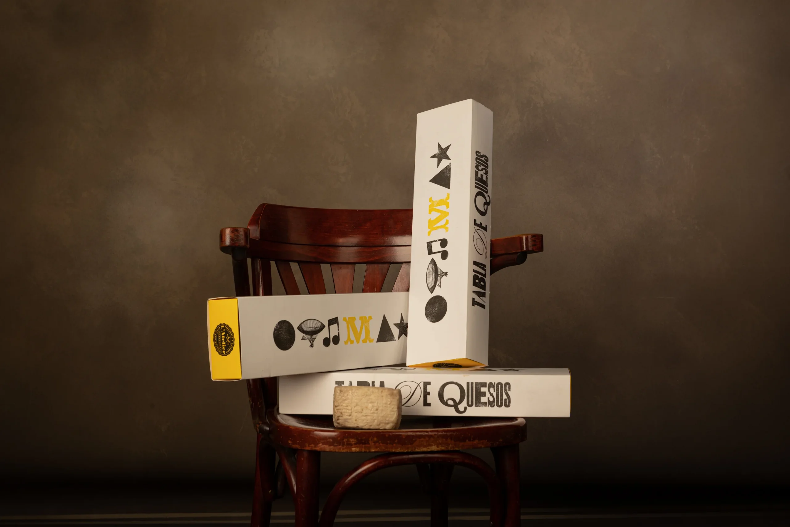 Imagen de varias cajas apiladas con detalle amarillo con el diseño de packaging de quesos L'Atelier con tipografía e iconografía de letterpress